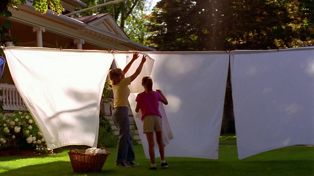 广角摄影车拍摄了在院子里晾衣服的女人+女孩和草地上的洗衣篮视频下载