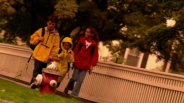 三个孩子穿着雨衣走在郊区的人行道上视频素材