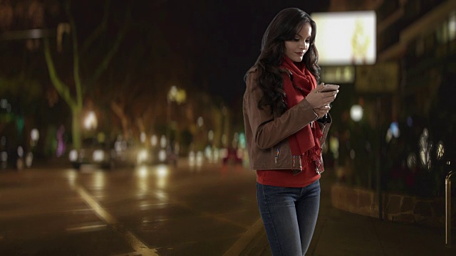 年轻女子晚上在街上用智能手机视频素材