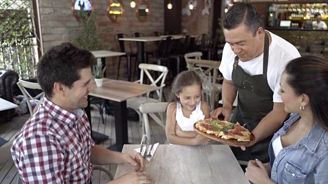 在一家餐馆里，服务员正在为一个美丽的家庭服务披萨视频素材