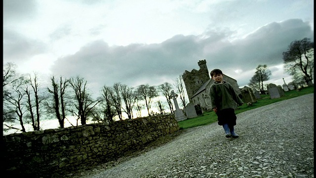 倾斜的低视角，小男孩扔石头站在乡村道路/教堂的背景/爱尔兰视频素材