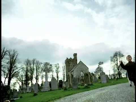 高对比三个男孩跑在乡村公路上向相机/教堂/墓地的背景/爱尔兰视频下载