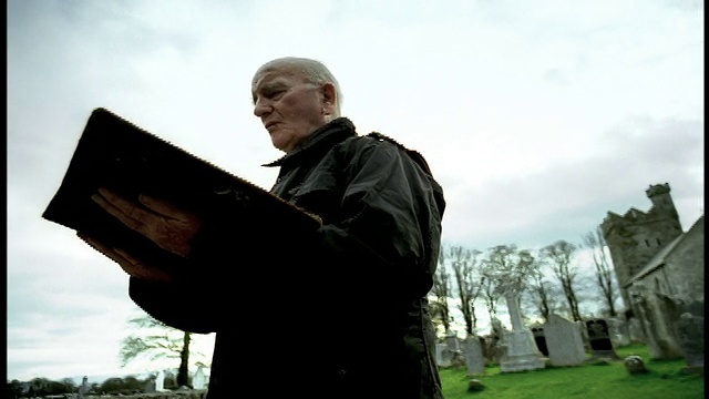低角度摄影车拍摄远离高级男子在墓地/爱尔兰中间读大书黑衣视频素材