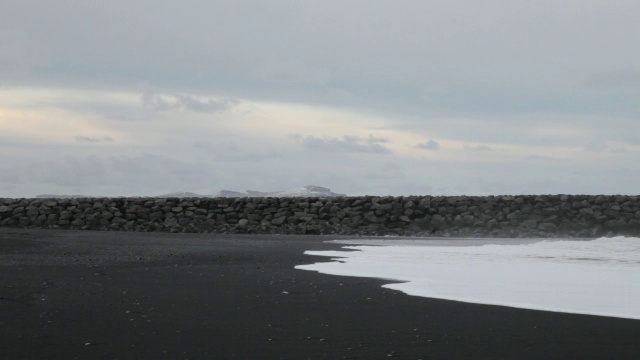 在冰岛Vik I Myrdal，海浪拍打着海滩，背景是一个防波堤视频素材