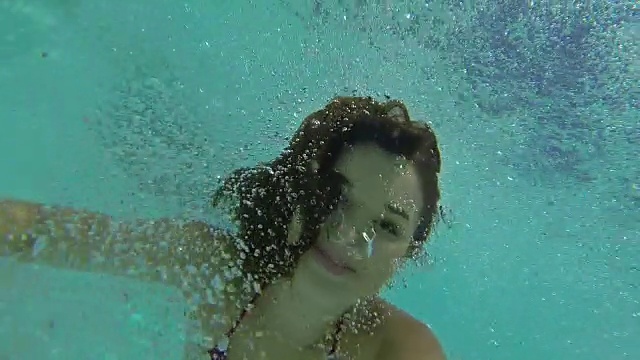 年轻女子微笑着在后院游泳池的水下游泳视频素材