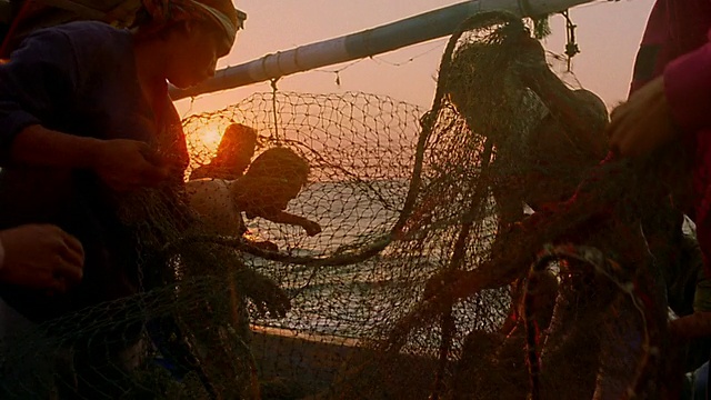 亚洲渔民在船上拉网/太阳在海洋上落下背景/爪哇，印度尼西亚视频下载