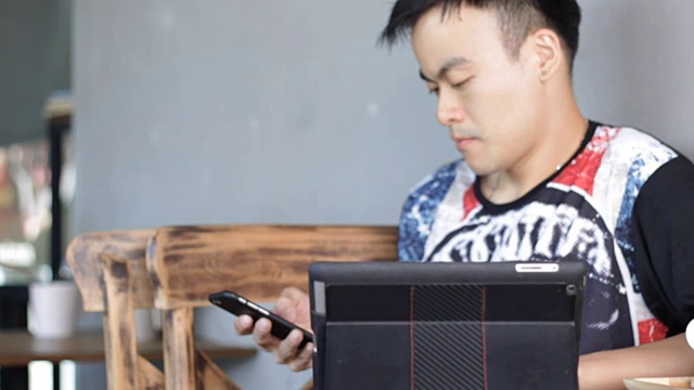 一名亚洲男子在咖啡店使用平板电脑和智能手机视频素材