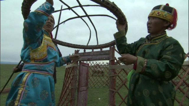 巴音布鲁克草原上，穿着传统服装的男子将蒙古包的顶棚圈装在长柱子上。视频下载