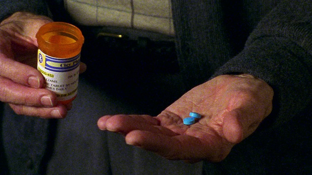 靠近老人的右手，将两粒蓝色药丸从瓶中倒入左手视频素材