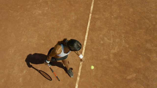在发球前，女子在红土场上弹跳网球的慢镜头视频素材