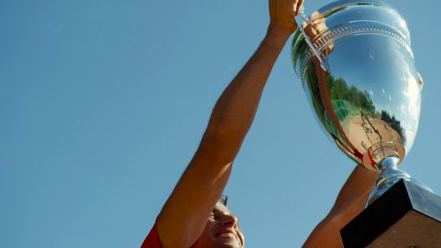 一个男人亲吻闪亮的网球奖杯并微笑着将奖杯举向天空的慢镜头视频素材