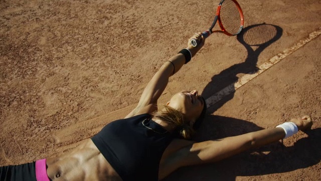 慢镜头头顶拍摄的女子躺在红土网球场上举起手臂庆祝胜利视频素材