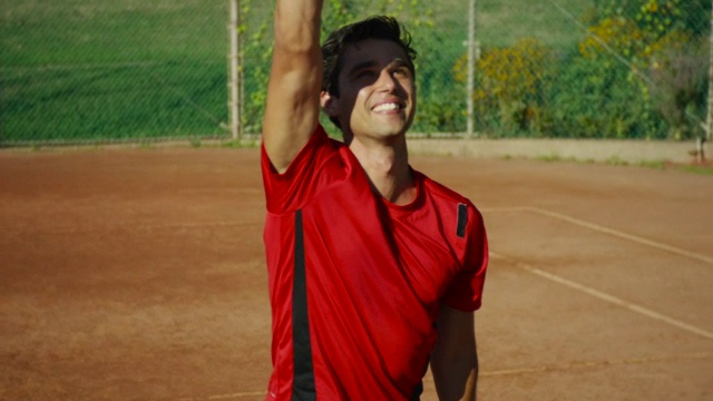 一个快乐的男人在网球场上亲吻他的球拍，并站起来庆祝胜利的慢动作镜头视频素材