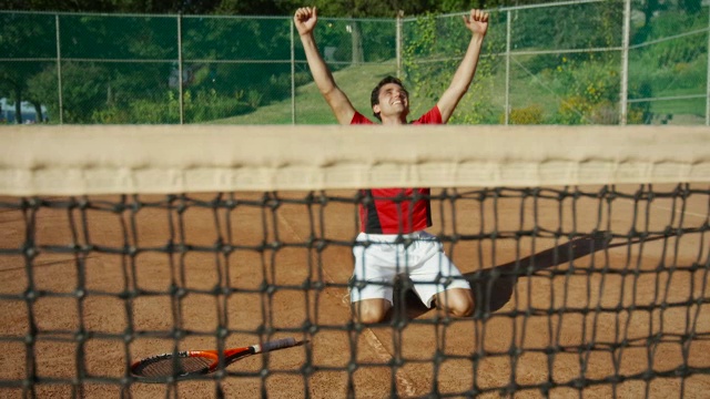 慢镜头拍摄的人跪在粘土网球场，举起手臂庆祝胜利视频素材