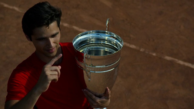 在红土网球场上，一名男子手持网球奖杯挥手致意视频素材