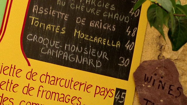 在普罗旺斯的咖啡馆里，倾斜的倾斜的锅架专注于法式黑板菜单和石头的“品酒”标志视频下载
