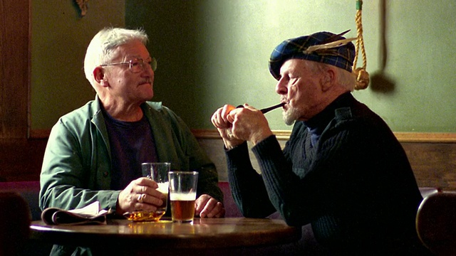两名中年男子坐在酒吧的桌子边喝着啤酒聊天/一个抽烟斗/新斯科舍省视频素材