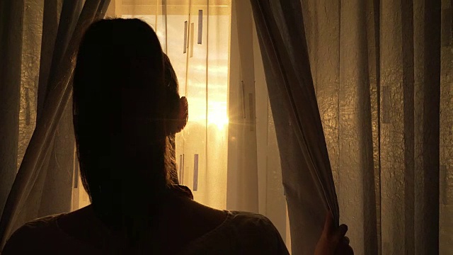 一个在窗边欣赏日落的女人。视频素材