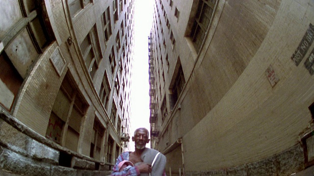在洛杉矶摩天大楼之间的小巷里，一个穿着敞开衬衫的成年黑人(无家可归者)视频素材