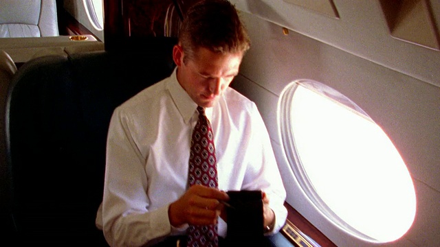摇摇晃晃的慢镜头，高角度，MS PAN过肩，商人在笔记本电脑上打字，面对在飞机上使用PDA的人视频素材
