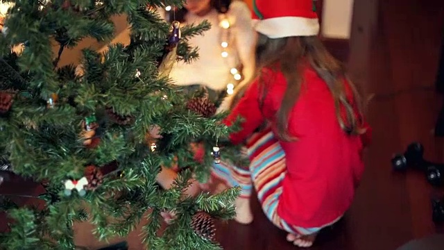的生活方式。女孩们在圣诞树旁摆弄圣诞彩灯视频素材