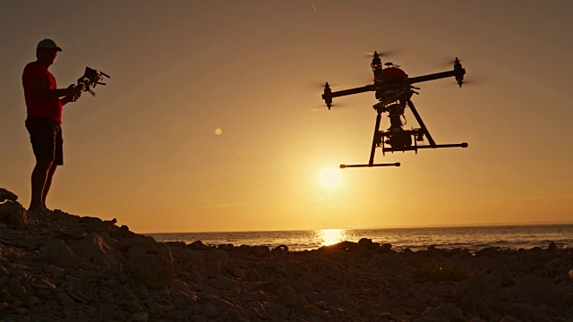 日落时分，一名男子操控无人机降落在海滩上视频素材