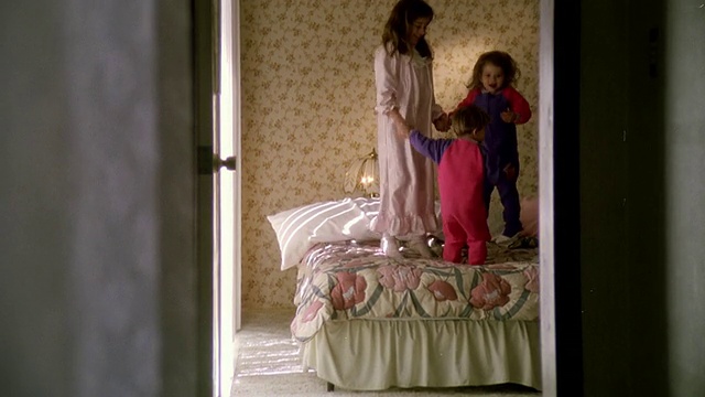 宽镜头三个穿着睡衣的孩子在床上跳/穿过门口拍视频素材