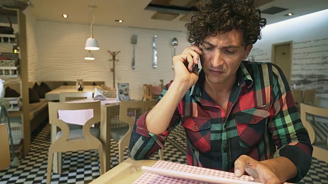 一个年轻人在咖啡店里使用手机和平板电脑。视频素材