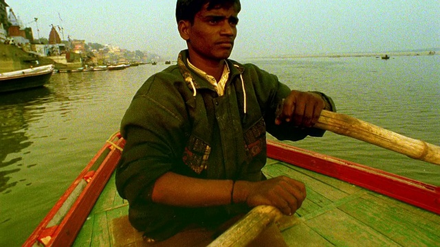 慢镜头宽镜头从船的角度看河岸上的城市/倾斜平底锅到划船的印度人/瓦拉纳西，印度视频下载