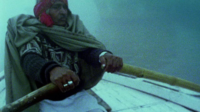 慢动作中镜头pan中年男子在迷雾中头饰划艇黄昏/瓦拉纳西，印度视频下载