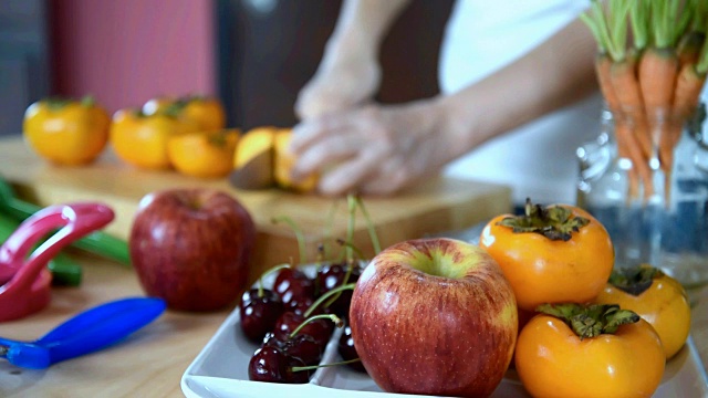 女人切柿子，各种水果在厨房/健康的生活方式概念视频下载