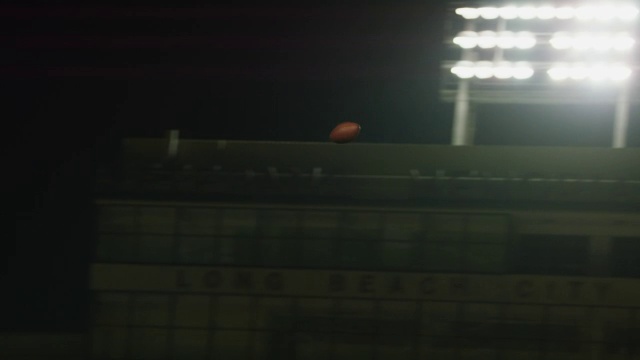 在明亮的体育场灯光下，盘旋的足球在球场上空翱翔。视频下载