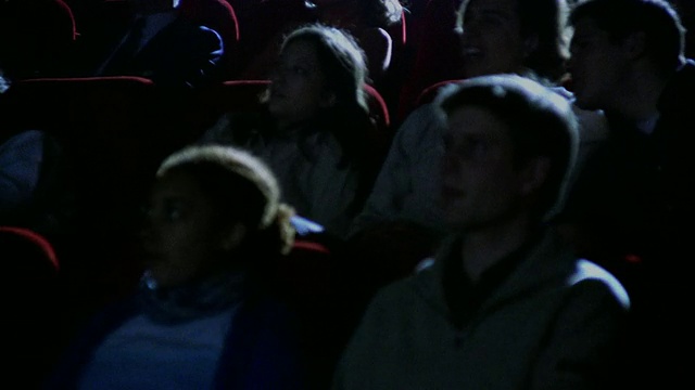 在黑暗的电影院里，中景摄影车经过专心观看电影的观众视频下载