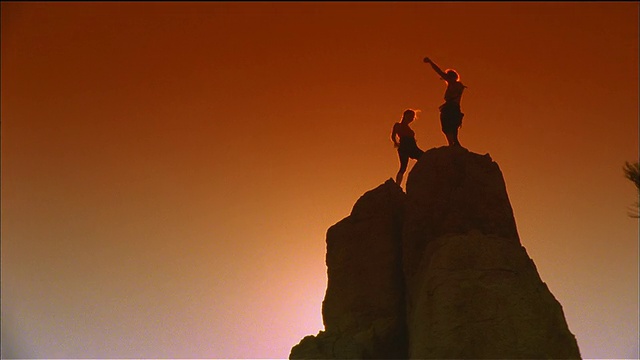 低角度广角长镜头剪影两名妇女在爬到顶端后在岩石上击掌/圣塔菲，新墨西哥州视频素材