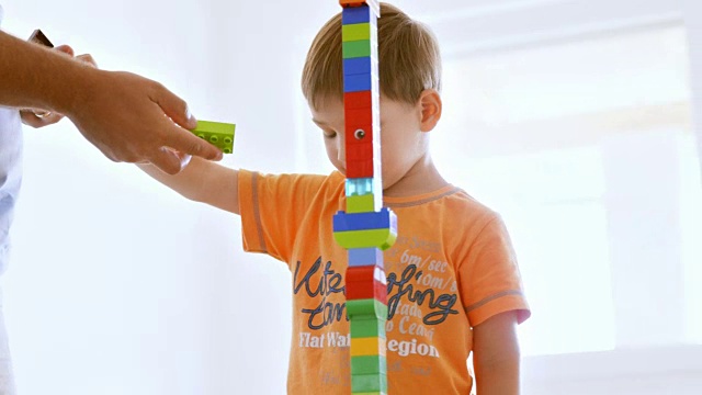 男孩和父亲一起建造一座高高的塑料砖塔视频下载