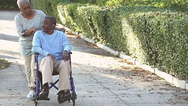 非裔美国老年妇女推着轮椅上的男人视频素材