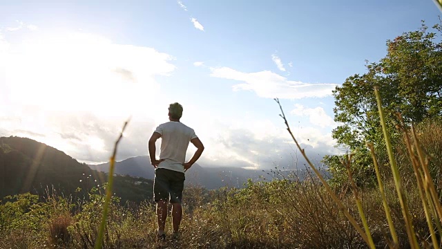 日出时，男性徒步者穿过山间的草地视频素材