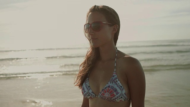 在法国南部的大西洋海滩上，穿着比基尼、戴着太阳镜的美女在欣赏风景视频下载