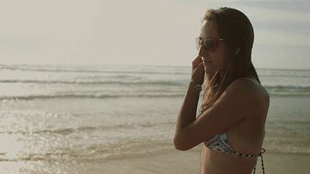 穿着比基尼戴着耳机的美女在法国南部的大西洋海滩上散步视频下载