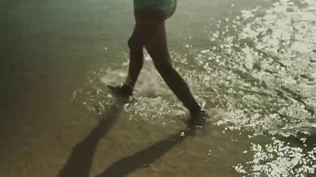 在法国南部的大西洋海滩上，美丽的女子穿着比基尼戴着耳机跳舞，在水中行走视频下载