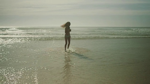 在法国南部的大西洋海滩上，美丽的女子穿着比基尼戴着耳机在水中跳舞视频下载