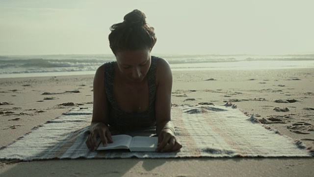 在法国南部大西洋的海滩上，美丽的女人在毯子上看书的肖像视频下载