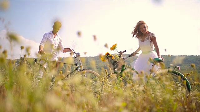 年轻浪漫的夫妇在田野里骑着自行车。视频下载