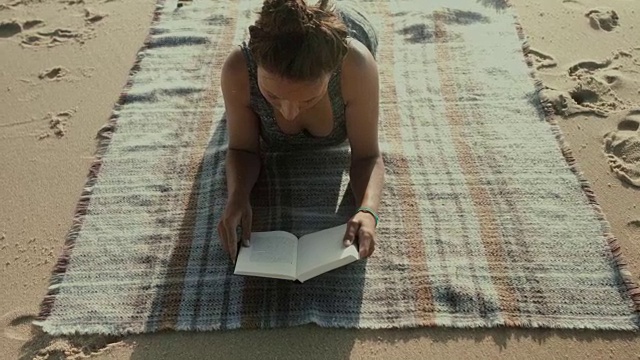 在法国南部大西洋的海滩上，一个漂亮的女人在毯子上看书视频下载