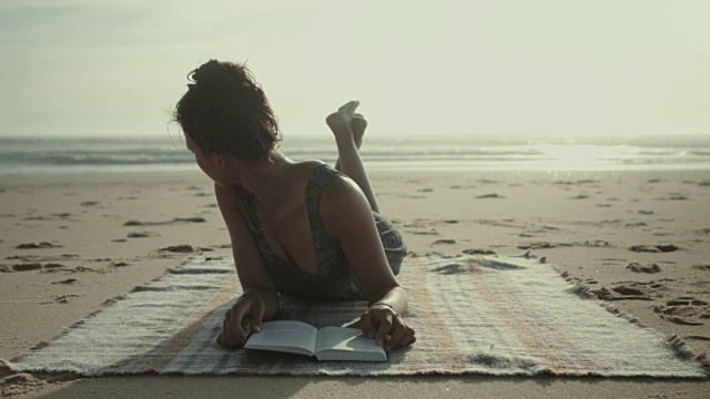 在法国南部大西洋的海滩上，一个漂亮的女人在毯子上看书视频下载