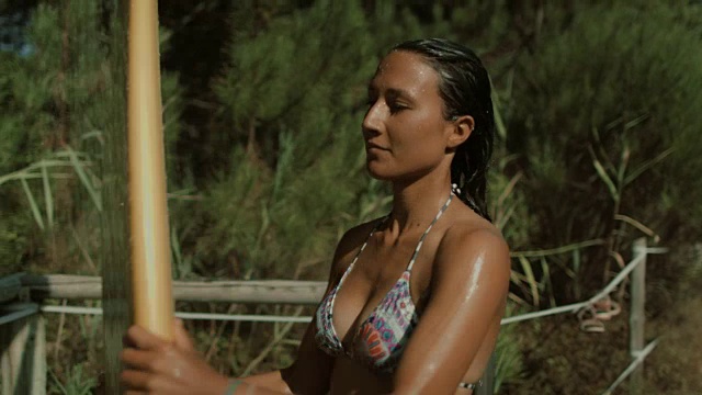 美丽的女性冲浪者洗澡的比基尼在海滩在夏天与冲浪板视频下载