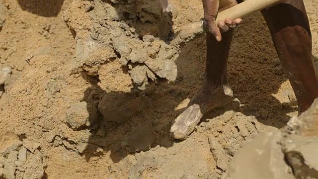 在塞拉利昂的一个钻石矿坑里，光着脚的男人铲沙子和泥浆的特写镜头。视频下载