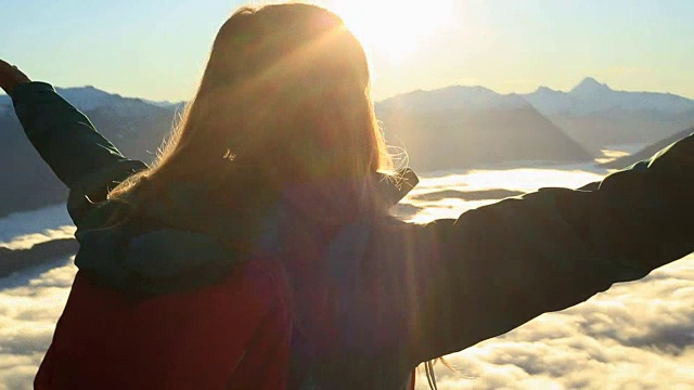 一名徒步的年轻女子站在云霄之上的山峰上，伸开双臂视频素材