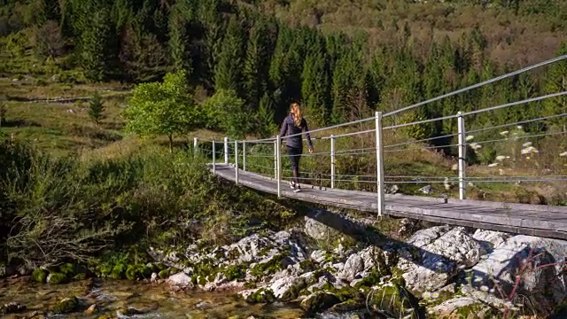 一名年轻女子正穿过山间溪流上的吊桥视频素材