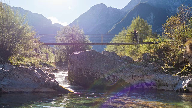 一名年轻女子正跑过山间溪流上的吊桥视频素材